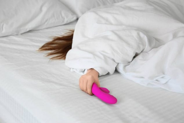 Girl under sheets using rabbit style vibrator adult toys